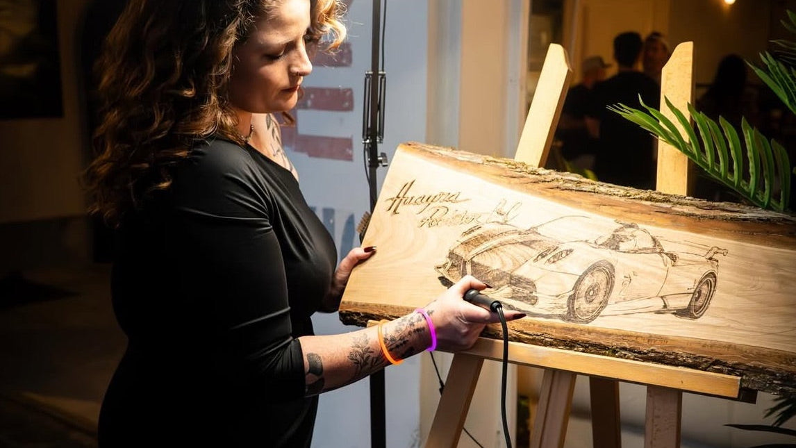 Woman wood burning a wooden board with an illustration of a Pagani using a ring light.